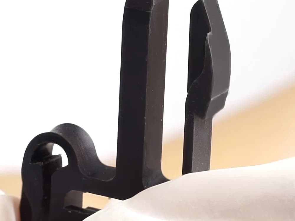 Nahaufnahme zweier schwarzer Clips aus ABS110, die ein helles Bauteil festhalten.
