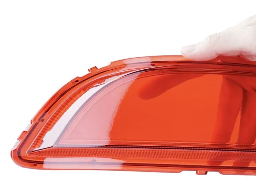 Eine behandschuhte Hand hält eine rot-orange, durchscheinende Leuchtenabdeckung aus Crysplus 1801.