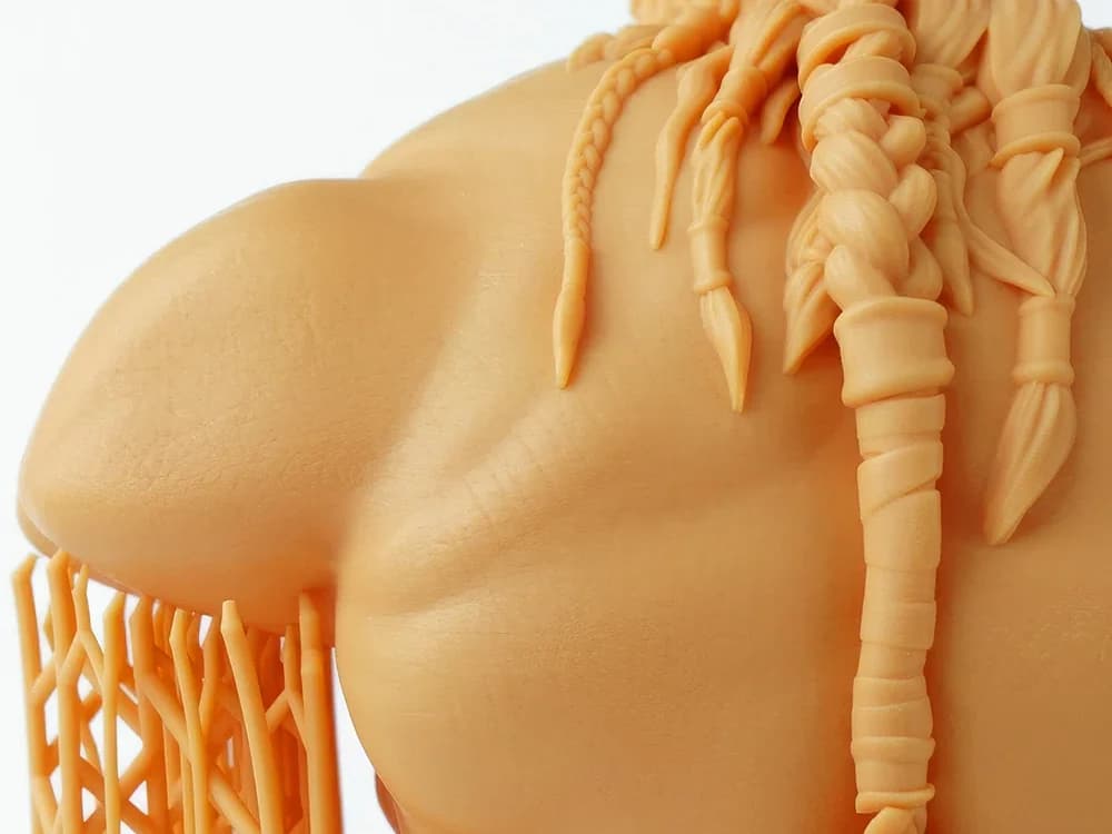 Nahaufnahme einer orangefarbenen Figur aus RC800, geflochtene Haarsträhnen und Stützstrukturen sind scharf ausgeformt.