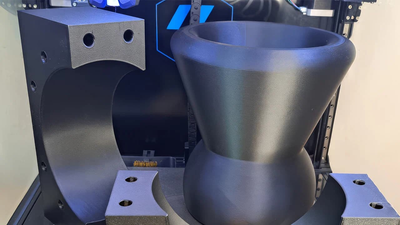 Mehrteilige schwarze 3D-gedruckte Komponenten auf Druckbett eines 3D-Druckers.