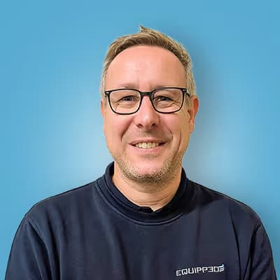 Lächelnder Mann mit Brille und kurzem Haar vor blauem Hintergrund, trägt ein dunkles Sweatshirt mit der Aufschrift ‚EQUIPP365‘.