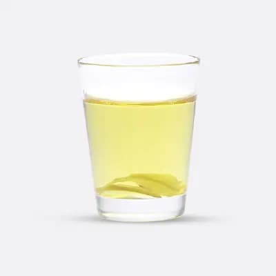 Glas mit hellgelbem Wasser und einem Teebeutel darin.