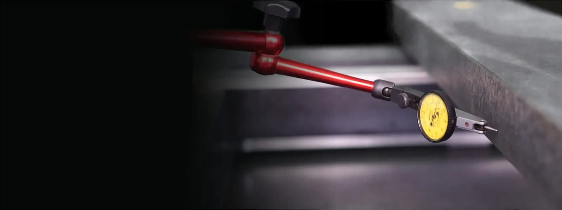 Messuhr mit gelbem Zifferblatt an einem roten Messarm, der die Dicke einer Metallplatte misst.
