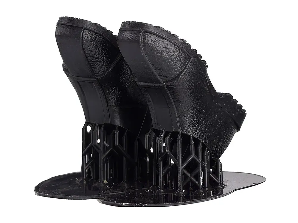 Zwei schwarze, glänzende Schuhsohlen aus ABS110, noch auf ihren gedruckten Stützstrukturen stehend.